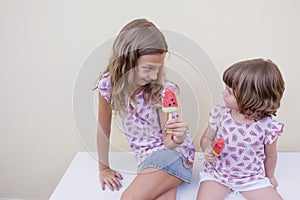 Two beautiful sister kids eating a watermelon ice cream. Family love and lifestyle outdoors