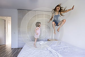 Two beautiful sister kids playing and jumping on bed at home. Fun indoors. Family love and lifestyle