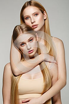 Two beautiful sister twins girls with same blonde long hair and perfect skin
