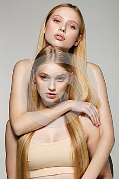 Two beautiful sister twins girls with same blonde long hair and perfect skin