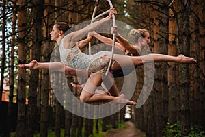 Two beautiful and slim gymnasts doing difficult exercises on aerial ring