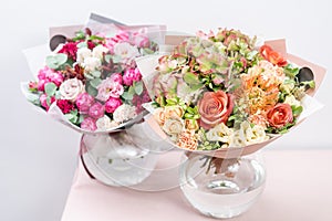 Two beautiful spring bouquet. flowers arrangements with various of colors in glass vase on pink table. bright room