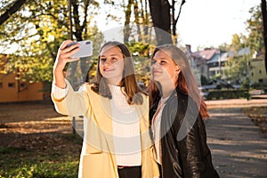 Two beautiful teen girls taking selfie on the phone while  in sunny autumn park