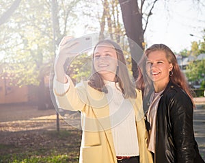 Two beautiful teen girls taking selfie on the phone in sunny autumn park