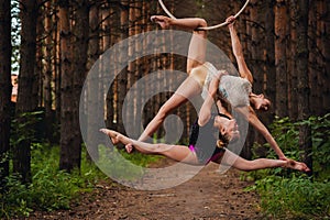 Two beautiful teen gymnasts doing exercises at the air ring in the woods