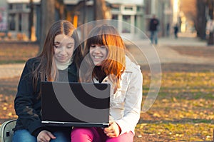 Two beautiful teenage girls having fun with notebook in the park