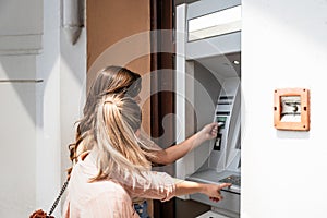 Two beautiful tourists female withdrawing the money from a bank card using ATM machine at the city center. Two travelers friend