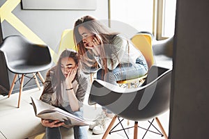 Two beautiful twin girls spend time read a book in library in the morning. Sisters relaxing in a cafe and having fun