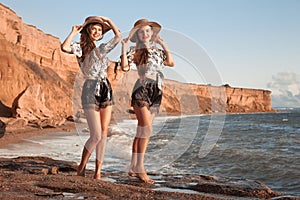 Two beautiful twins girl in straw hat having fun on the beach enjoying life, summer sunset outdoor portrait. People Girlfriend