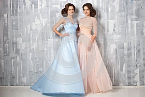 Two beautiful twins young women in luxury dresses, pastel colors