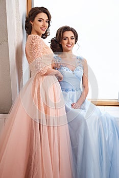 Two beautiful twins young women in luxury dresses, pastel colors