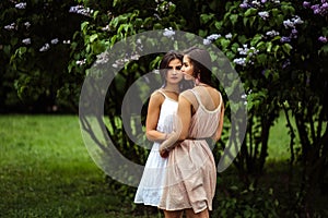 Two beautiful twins young women in summer dresses near blooming lilac