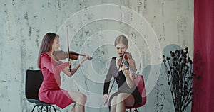 Two beautiful violinists perform the music on beautiful background indoor. 4K