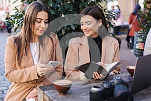 Two beautiful woman sitting in cafe and working. Woman checking free dates and planing. Professional photography career