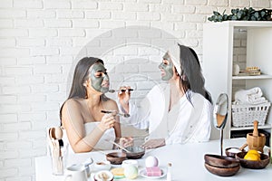 Two beautiful women applying facial mask having fun