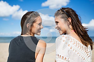 Two beautiful women on beach looking at each other laughing