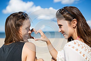 Two beautiful women on beach making heart shape laughing