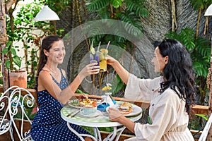 two beautiful women friends clinking lemonades for cheers and eating breakfast in cafe