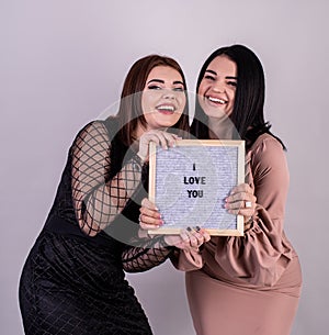 Two beautiful women holding a felt letter board with the words I Love You on gray background