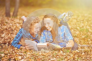 Two beautiful women lying on leaves and reading books in autumn park. Education, friendship lifestyle concept