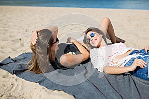 Two beautiful women lying together on beach laughing