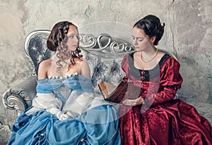 Two beautiful women in medieval dresses on the sofa reading book