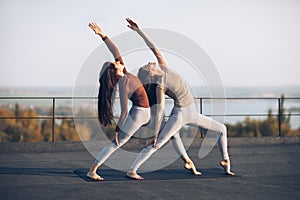 Two beautiful women perform double pose warrior with raised hand