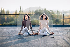 Two beautiful women perform meditative pose gomukhasana