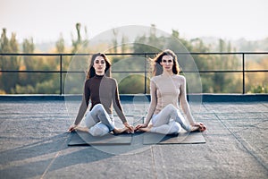 Two beautiful women perform meditative pose on the roof