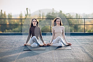 Two beautiful women perform meditative pose on the roof photo