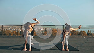 Two beautiful women practicing yoga pose on the roof, outdoors in morning