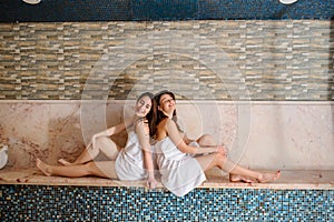 Two beautiful women wearing white towels relaxing in hamam