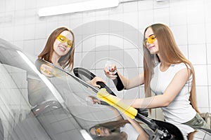 Two beautiful women worker washing windshield with sponge on car wash, window clean from dirt eco spray polishing