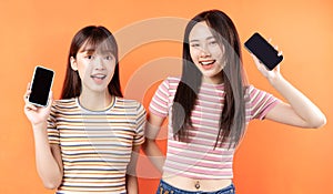 Two beautiful young asian girls are using mobile phones on orange background