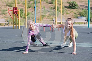 Two beautiful, young and athletic girls doing push-ups on a street playground.