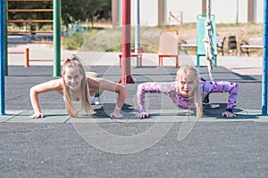 Two beautiful, young and athletic girls doing push-ups on a street playground.
