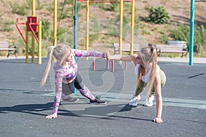 Two beautiful, young and athletic girls doing push-ups on a street playground.