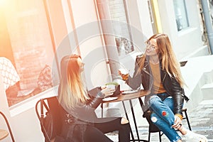 Two beautiful young blonde women drinking coffee and gossiping in nice restaurant outdoor