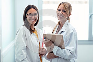 Two beautiful young female doctor holding digital tablet while smiling looking at camera in hospital