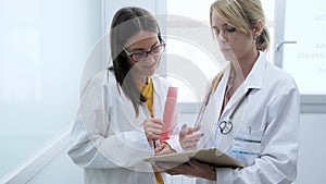 Two beautiful young female doctors talking each other while holding digital tablet in hospital.