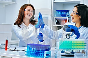 Two beautiful young female scientists working in laboratory and giving high five to each other