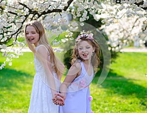 Beautiful young girls with blue eyes in a white dresses in the garden with apple trees blosoming having fun and enjoying smell of