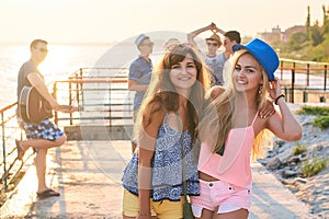 Two beautiful young girls having fun at the evening seaside with group of their friends on background