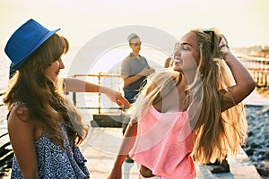 Two beautiful young girls having fun at the evening seaside with group of their friends on background