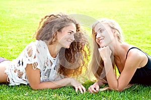 Two beautiful young girls with long curly hair lie on the grass on a summer day