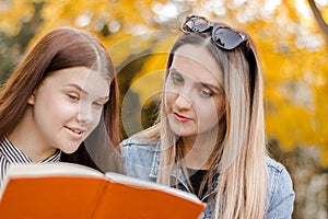 Two beautiful young girls, with pleasure, read a book in the autumn park