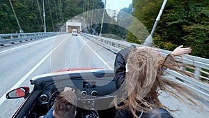 Two beautiful young girls ride in a red cabriolet among the mountains. Road on the highway. Dressed in black leather