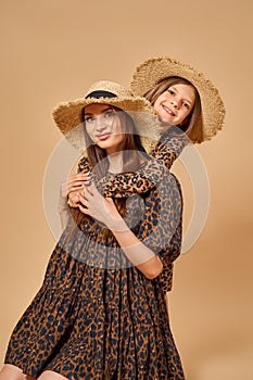 Two beautiful young girls sisters in nice animal pattern dresses with straw hats posing in studio