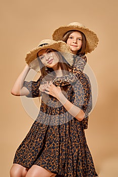 Two beautiful young girls sisters in nice animal pattern dresses with straw hats posing in studio