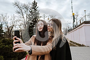 Two beautiful young girls take a selfie while walking in the park.